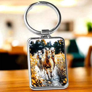 Porte-clés métallique avec image de trois chevaux sauvages galopant dans l'eau.
