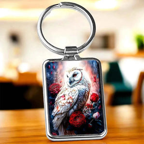 Porte-clés rectangulaire argenté avec motif hibou blanc et roses rouges.