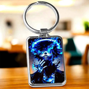 Porte-clés rectangulaire argenté avec une image d'un personnage masculin aux cheveux noirs et aux yeux invisibles entourés de flammes bleues, portant une veste noire et un collier argenté.