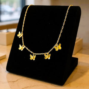 Collier Papillon Or avec pendentifs papillons délicats en or présenté sur un support noir élégant